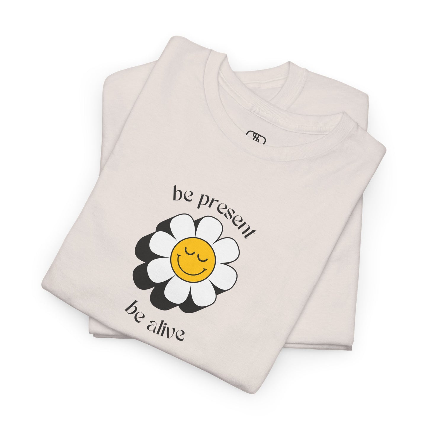 A vibrant yellow sunflower graphic on a folded t-shirt. The inspirational phrase “Be Present, Be Alive” is elegantly integrated into the design.