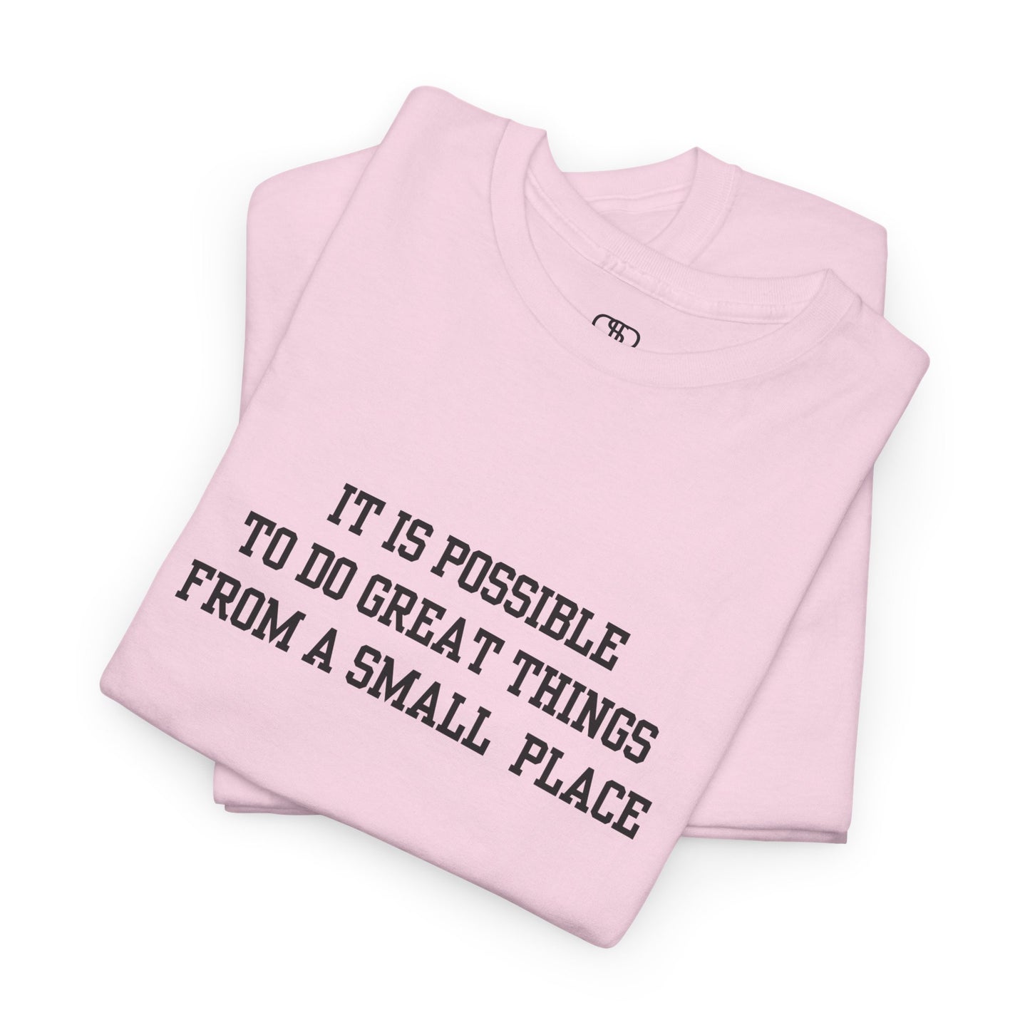 A folded light pink t-shirt with the quote “It is possible to do great things from a small place” on the front.