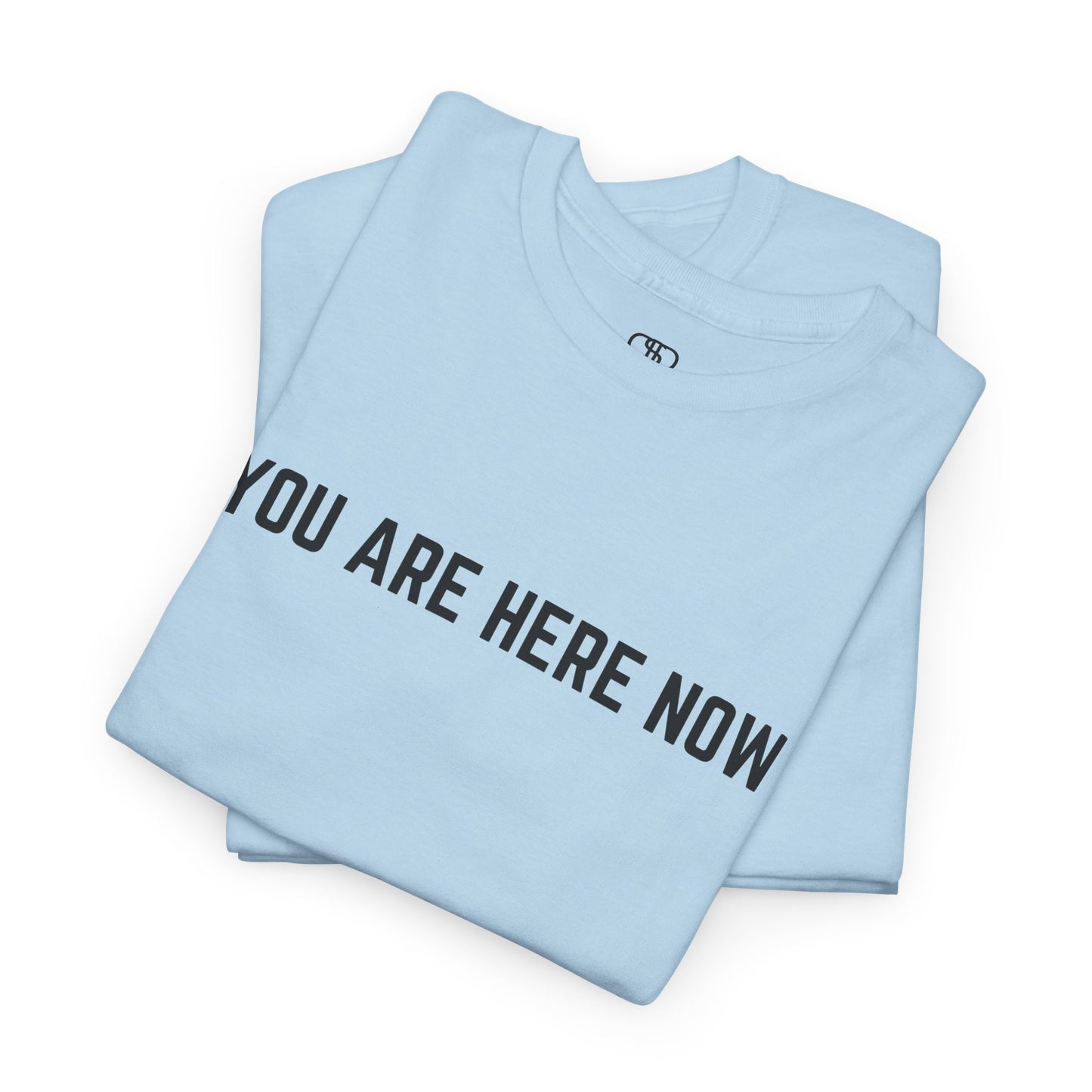 A folded t-shirt with the words "You are Here Now."