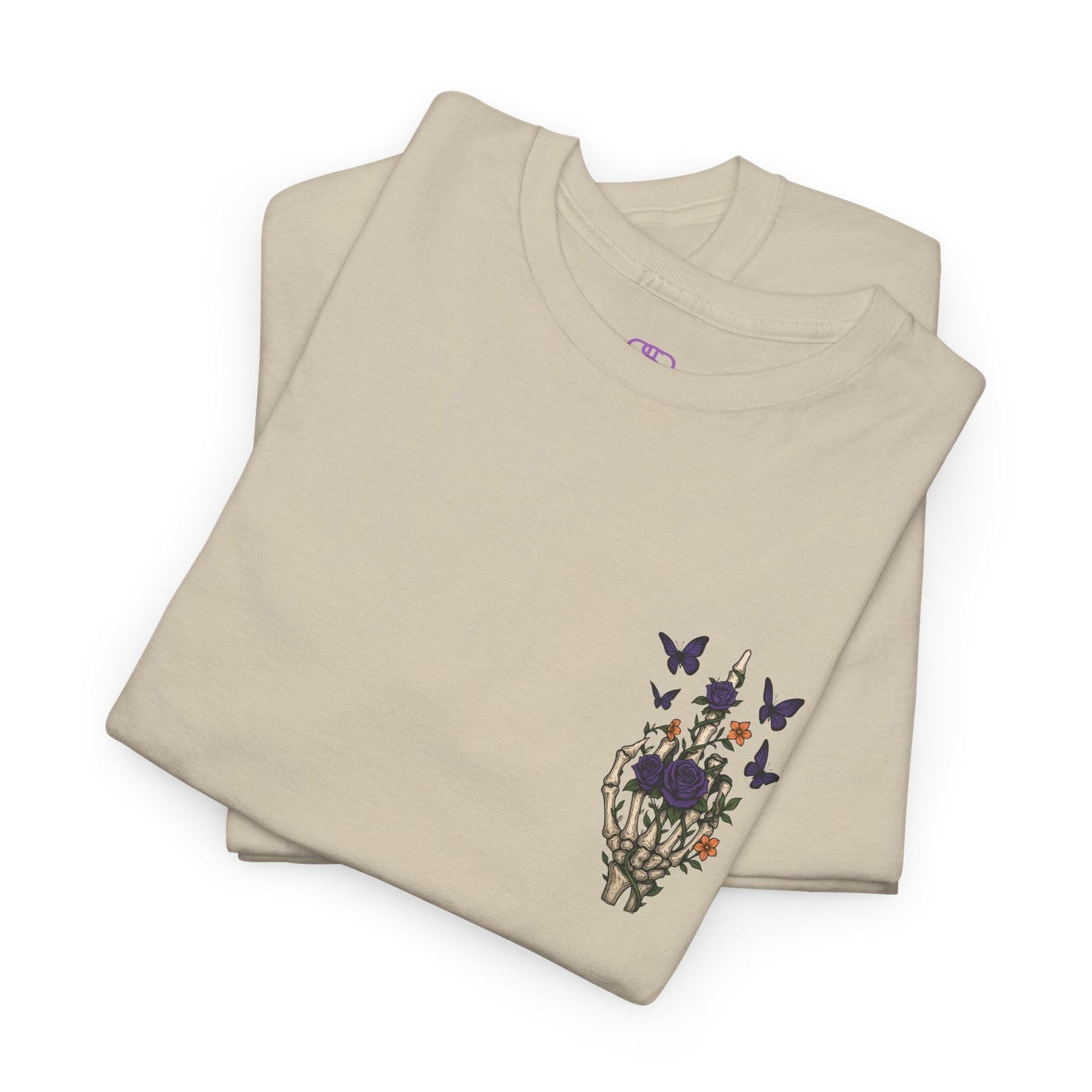 A folded sand t-shirt with a skeleton hand flipping its middle finger on the front surrounded by vines, roses, & butterflies, and a full skeleton design on the back with the phrase “My Last Flying Fuck.”