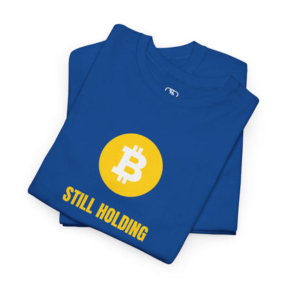 A folded royal blue  T-shirt with a Bitcoin emblem and "Still Holding" text in gold.