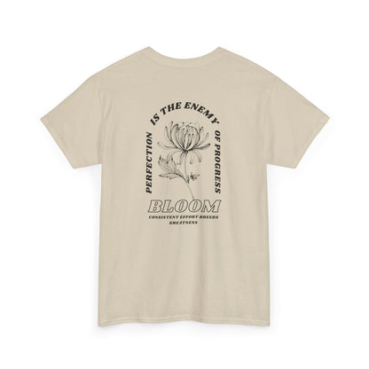 A [sand] t-shirt with a central flower design and the words “Perfection is the enemy of progress” and “Bloom” underneath it the phrase "Consistent effort breeds greatness," featured on the back of the t-shirt.