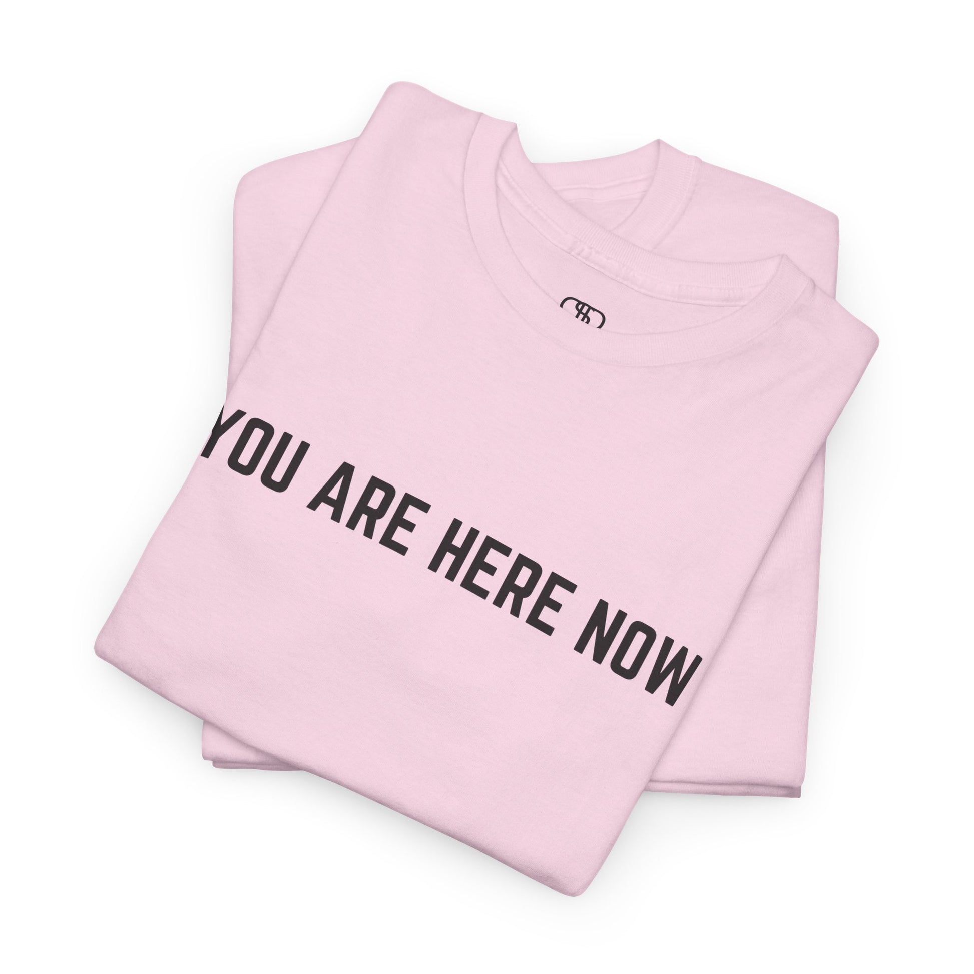 A folded light pink t-shirt with the words "You are Here Now." 
