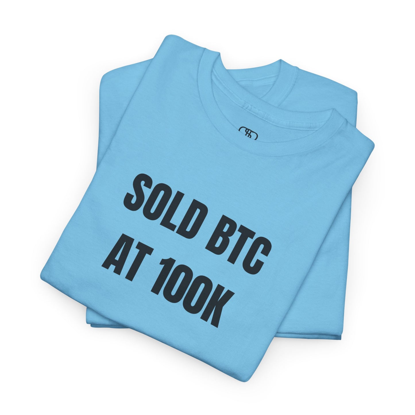A folded sky blue T-shirt with bold text "SOLD BTC At 100K" on the front.