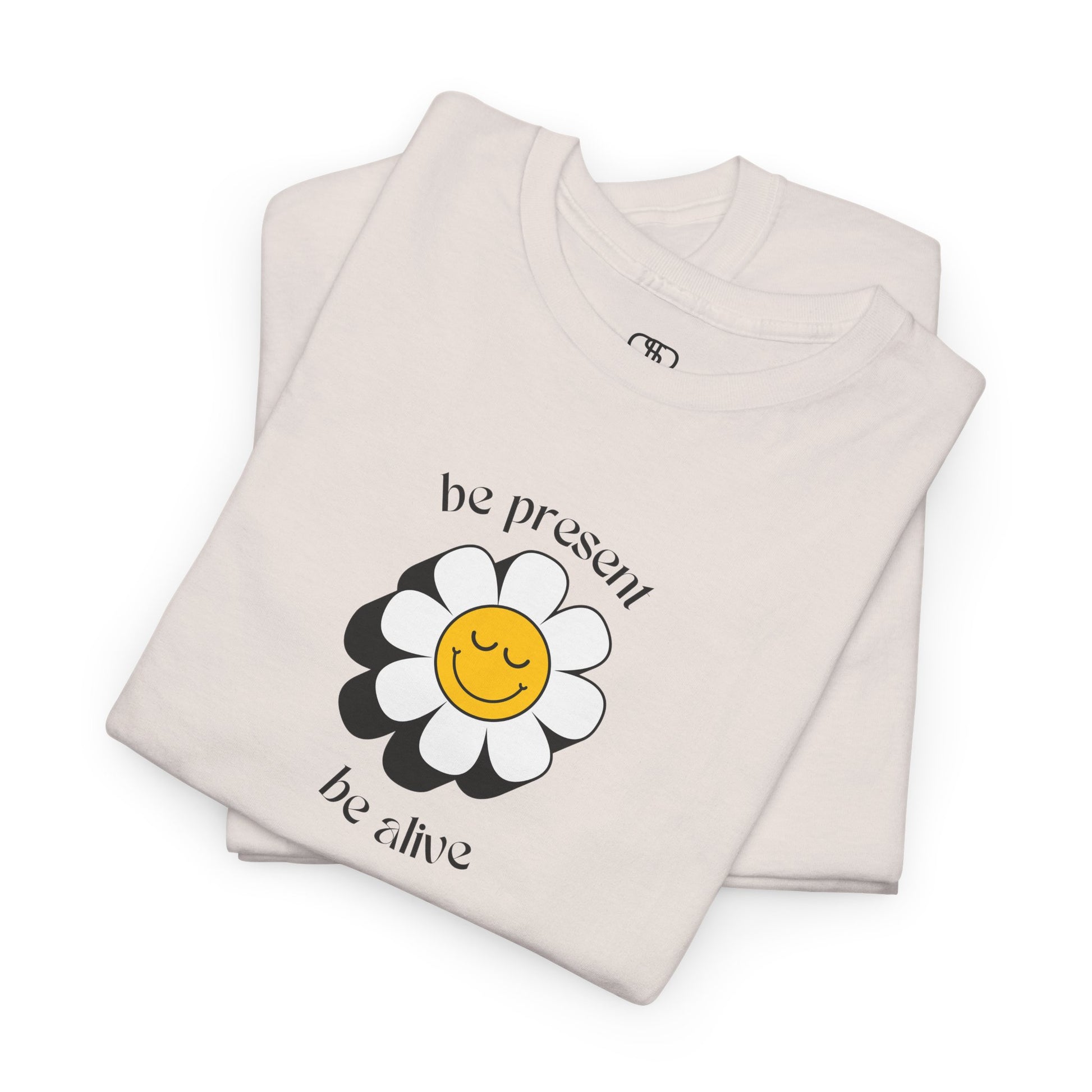 A vibrant yellow sunflower graphic on a folded t-shirt. The inspirational phrase “Be Present, Be Alive” is elegantly integrated into the design.