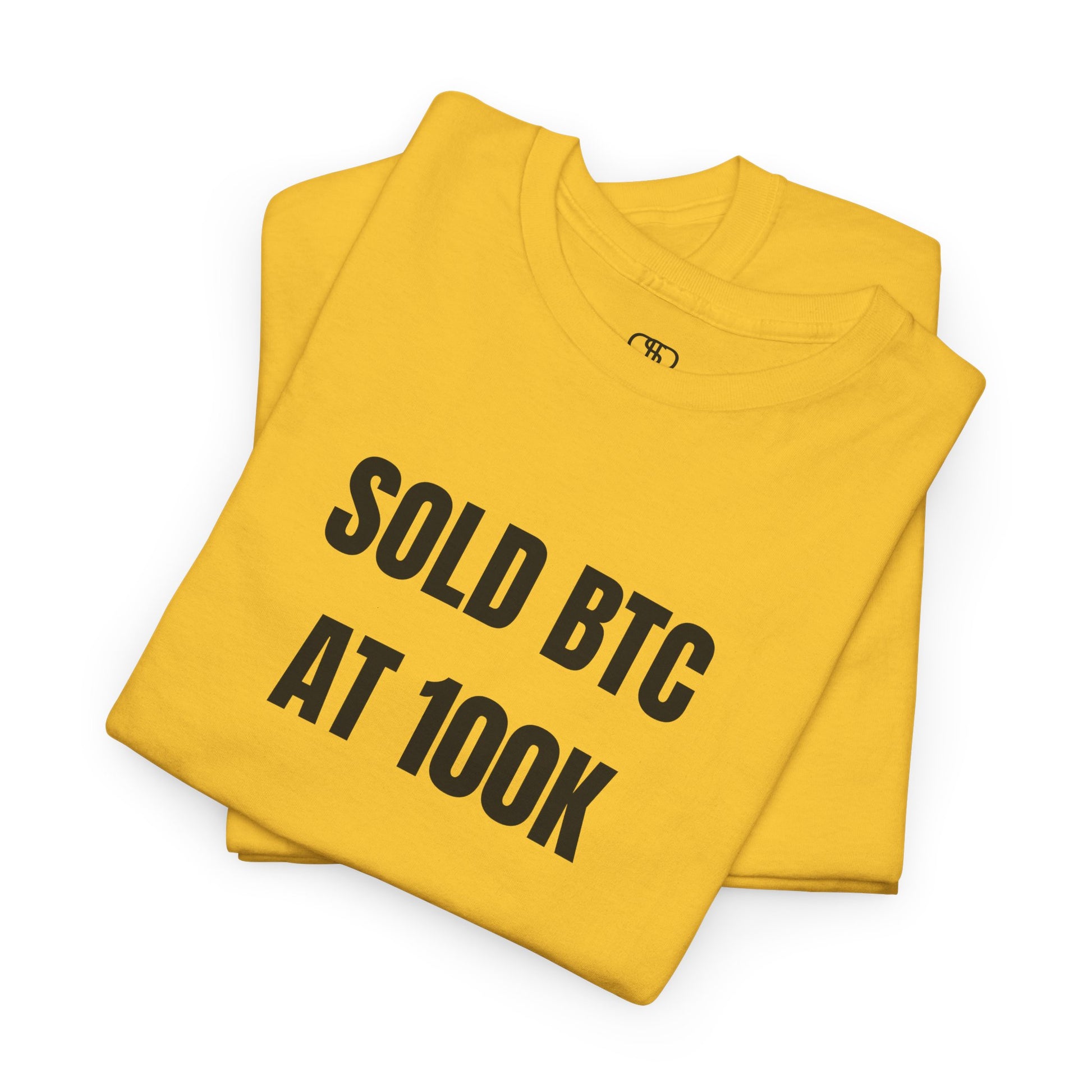 A folded daisy yellow T-shirt with bold text "SOLD BTC At 100K" on the front.