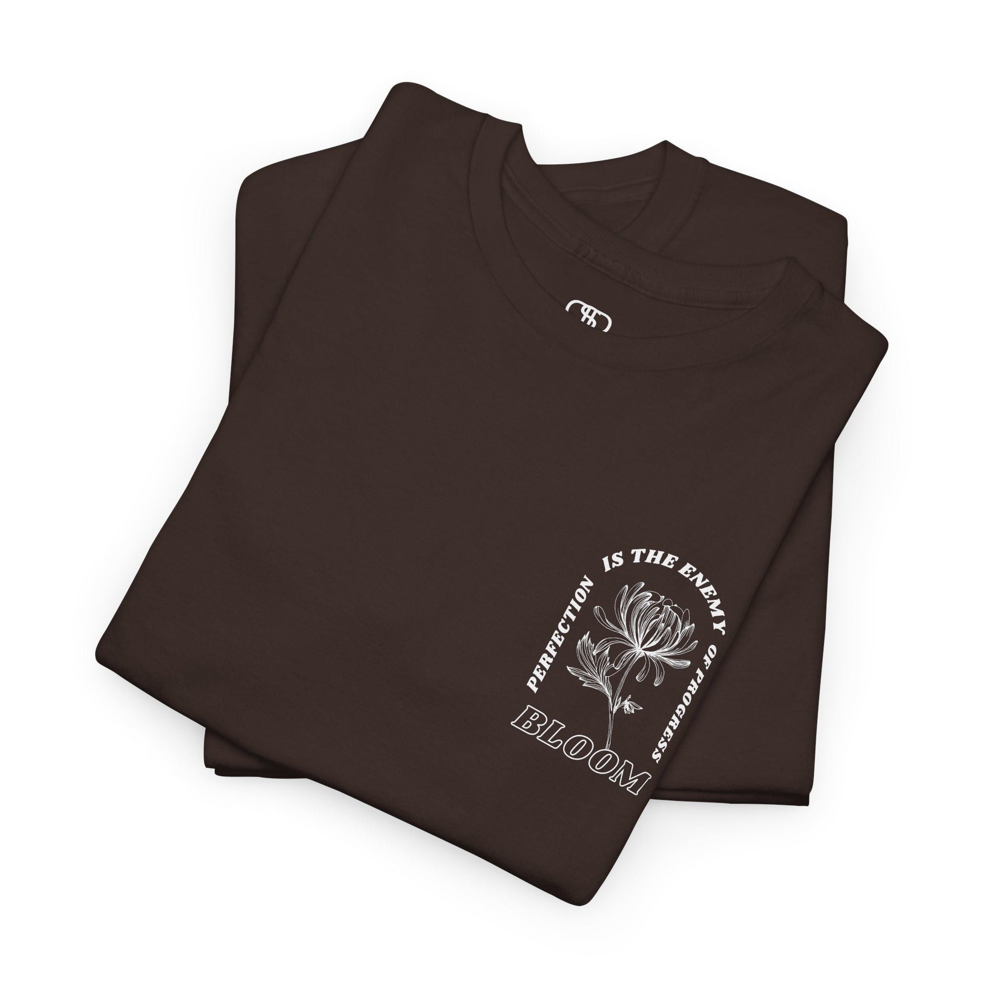 A [folded dark brown] t-shirt with a central flower design and the words “Perfection is the enemy of progress” and “Bloom” underneath it the phrase "Consistent effort breeds greatness," featured on the back of the t-shirt.
