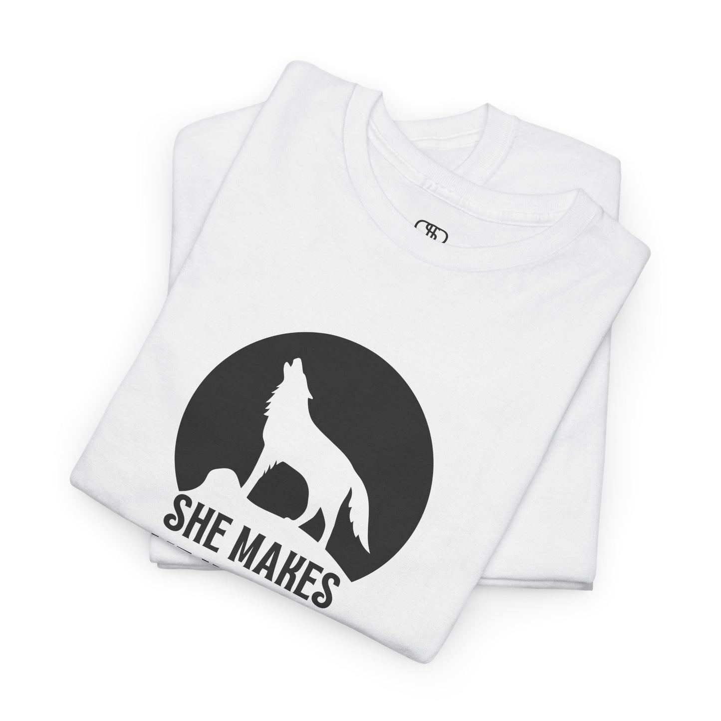 A folded white T-shirt with a wolf silhouette howling at the moon on a cliff, and "She makes me HOOWWL" text.