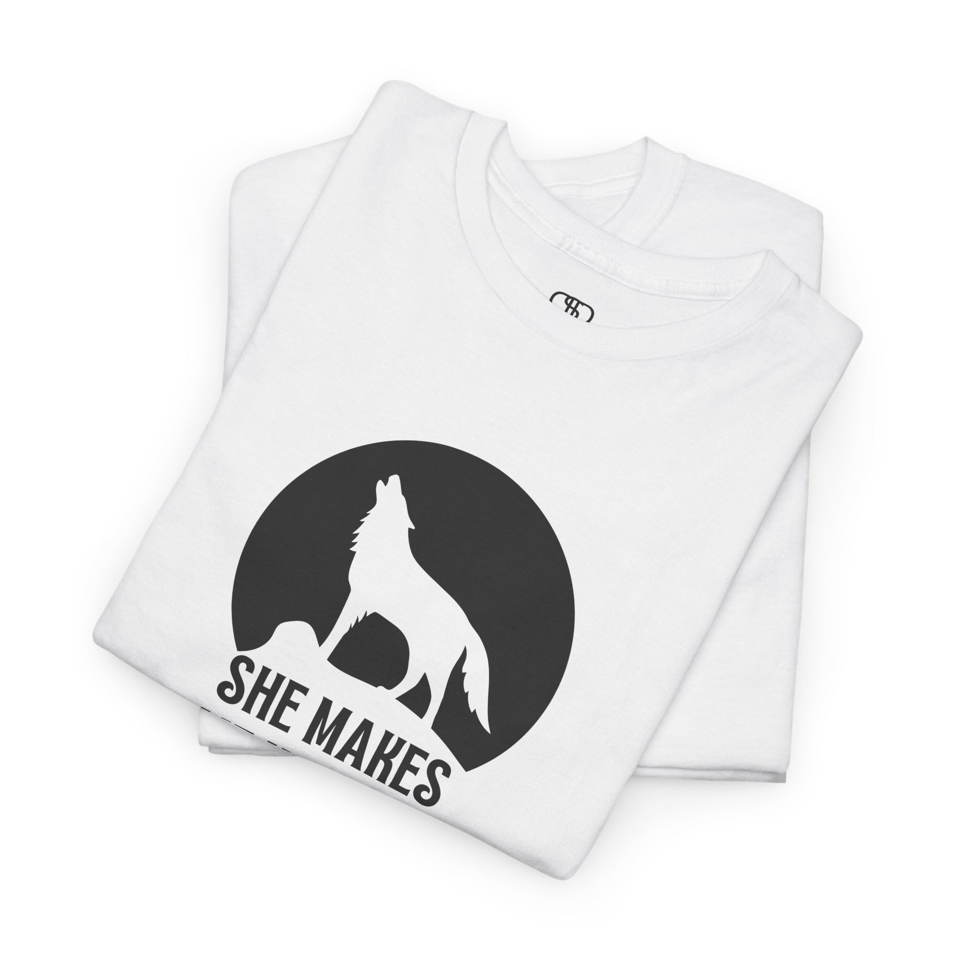 A folded white T-shirt with a wolf silhouette howling at the moon on a cliff, and "She makes me HOOWWL" text.
