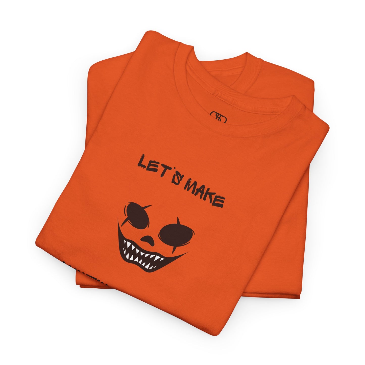 A folded orange T-shirt with a daring clown graphic with sharp teeth and scars, and "Let’s Make Haunting Memories" text.