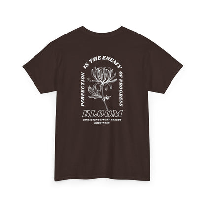 A [dark brown] t-shirt with a central flower design and the words “Perfection is the enemy of progress” and “Bloom” underneath it the phrase "Consistent effort breeds greatness," featured on the back of the t-shirt.