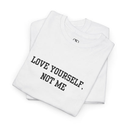 A folded minimalist t-shirt with the bold, centered text "Love yourself, not me" in a clean, modern font.