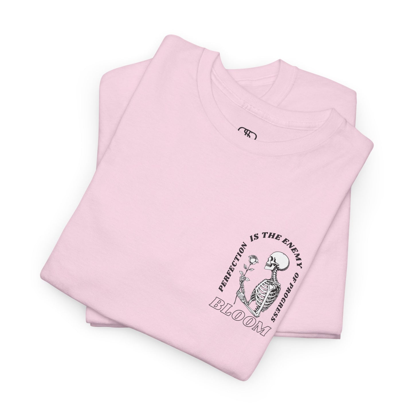 A [folded light pink] t-shirt with a central skeleton and rose design and the words “Perfection is the enemy of progress” and “Bloom” on the front.