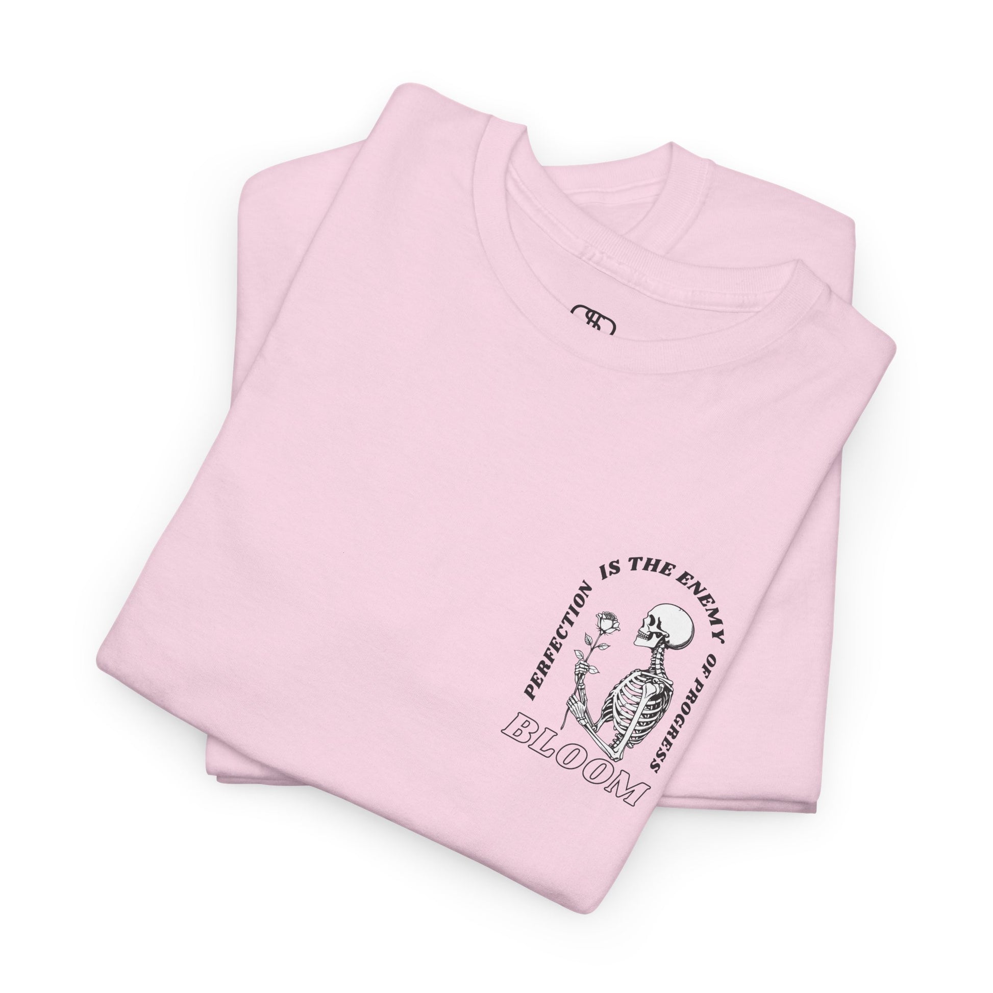 A [folded light pink] t-shirt with a central skeleton and rose design and the words “Perfection is the enemy of progress” and “Bloom” on the front.