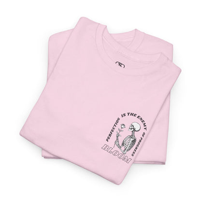 A [folded light pink] t-shirt with a central skeleton and rose design and the words “Perfection is the enemy of progress” and “Bloom” on the front.