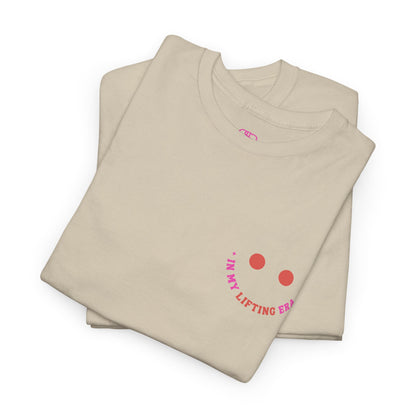 A folded sand  t-shirt with a retro smiley face on the front and the phrase “In my lifting Era” in a creative retro design on the back.