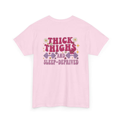 A [light pink] t-shirt with the phrase "Thick Thighs and Sleep Deprived" in a retro font on the front left and enlarged on the back.