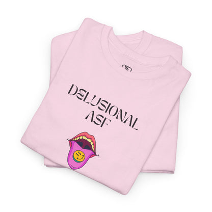 A folded light pink T-shirt with "Delusional asf" text, an open mouth graphic with tongue out, and a happy face emoji pill.