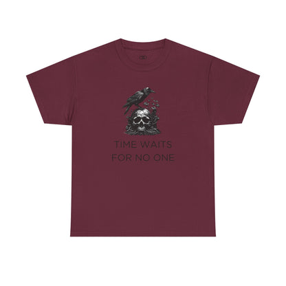 A close-up of a t-shirt with a gothic illustration. A black crow stands atop a weathered skull, which has moss and delicate vines growing through its eye sockets and around its form, blending nature and death.