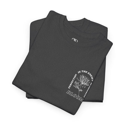 A [folded heather gray] t-shirt with a central flower design and the words “Perfection is the enemy of progress” and “Bloom” underneath it the phrase "Consistent effort breeds greatness," featured on the back of the t-shirt.