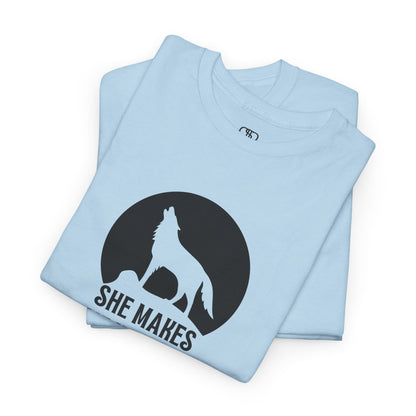 A folded light blue T-shirt with a wolf silhouette howling at the moon on a cliff, and "She makes me HOOWWL" text.