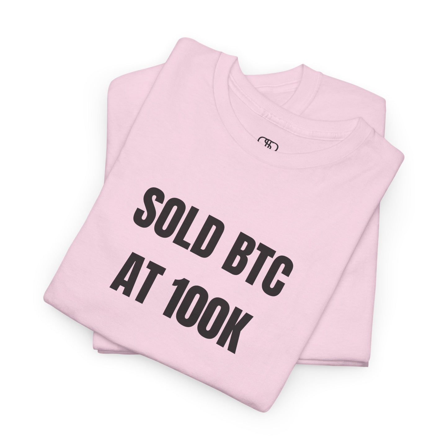 A folded light pink T-shirt with bold text "SOLD BTC At 100K" on the front.
