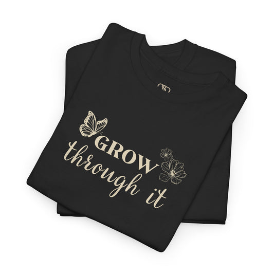 A folded black t-shirt with "Grow Through It" and a butterfly on the front and a design of a spine with vines, flowers, and butterflies on the back.