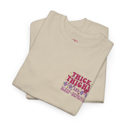 A folded [sand] t-shirt with the phrase "Thick Thighs and Sleep Deprived" in a retro font on the front left and enlarged on the back.