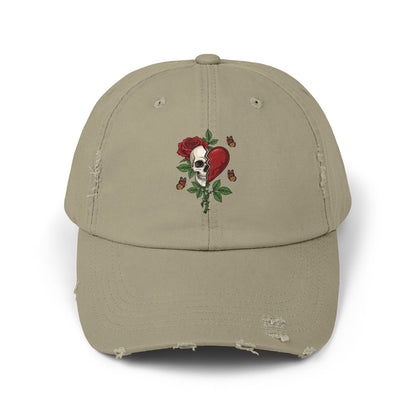 A distressed hat with an embroidered design of a half-skull and half-heart, split by a tear. A rose grows from the skull, surrounded by thorns and butterflies.