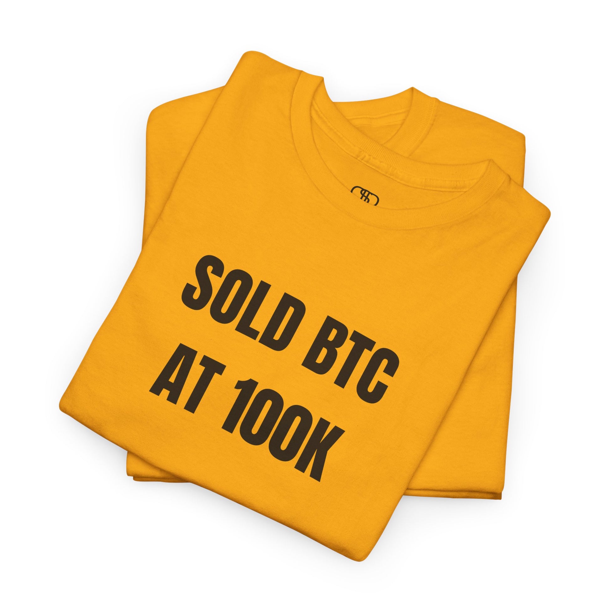 A folded gold T-shirt with bold text "SOLD BTC At 100K" on the front.