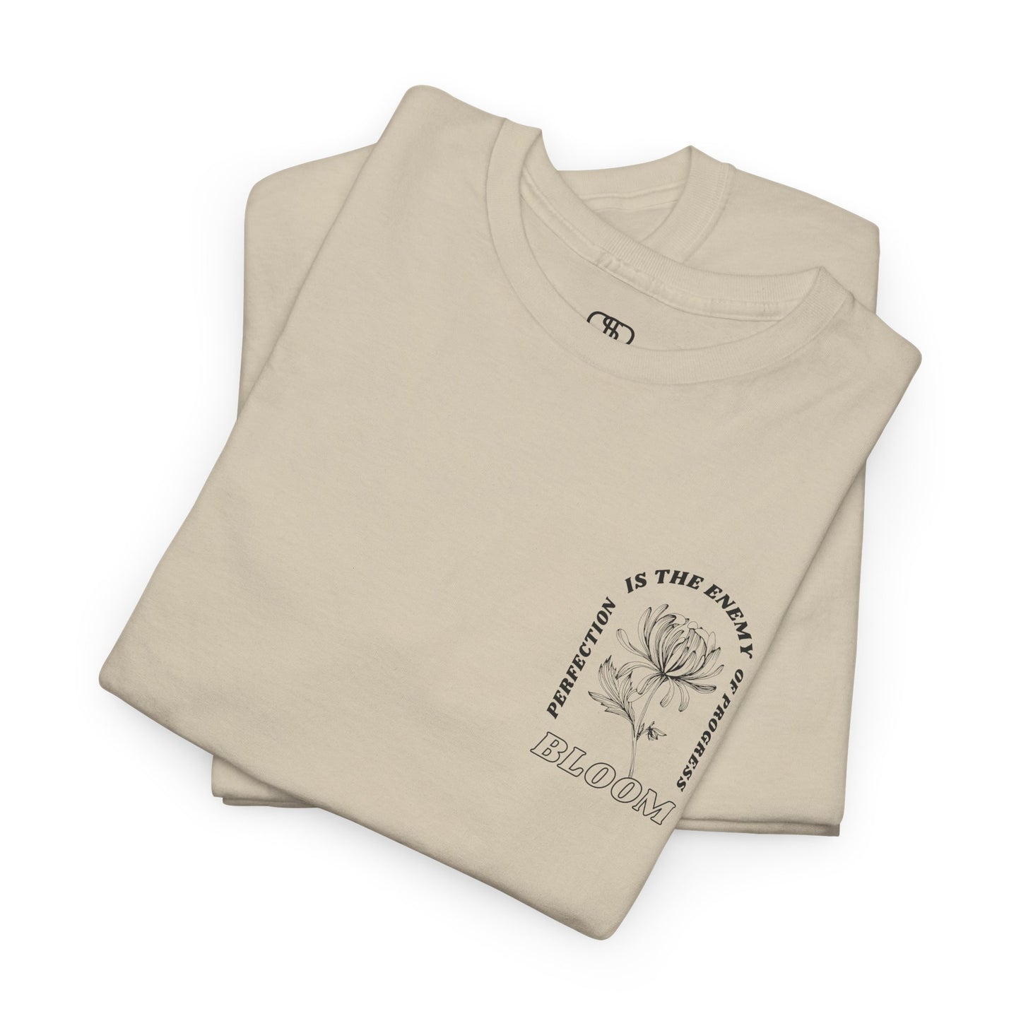 A [folded sand] t-shirt with a central flower design and the words “Perfection is the enemy of progress” and “Bloom” underneath it the phrase "Consistent effort breeds greatness," featured on the back of the t-shirt.