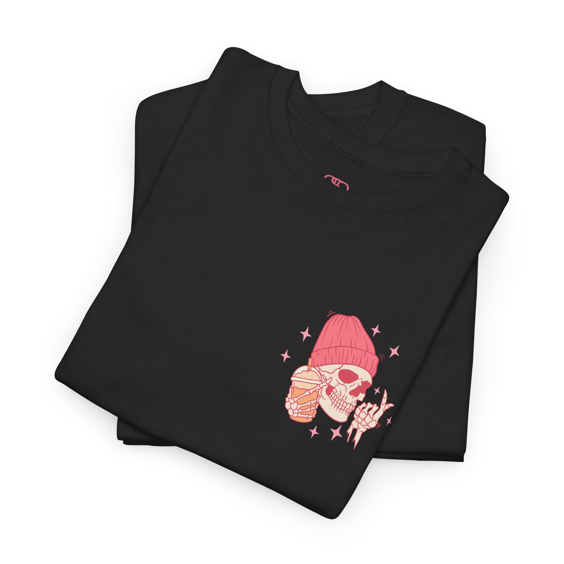 A black folded T-shirt with a skeleton in a pink beanie holding a frozen coffee, snapping fingers, surrounded by sparkles graphic.