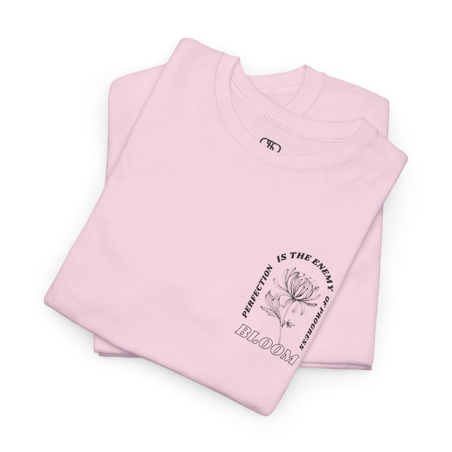 A [folded light pink] t-shirt with a central flower design and the words “Perfection is the enemy of progress” and “Bloom” underneath it the phrase "Consistent effort breeds greatness," featured on the back of the t-shirt.