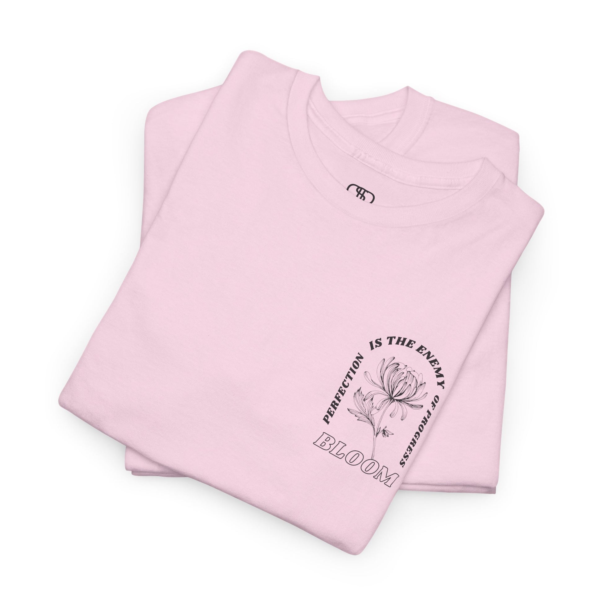 A [folded light pink] t-shirt with a central flower design and the words “Perfection is the enemy of progress” and “Bloom” underneath it the phrase "Consistent effort breeds greatness," featured on the back of the t-shirt.