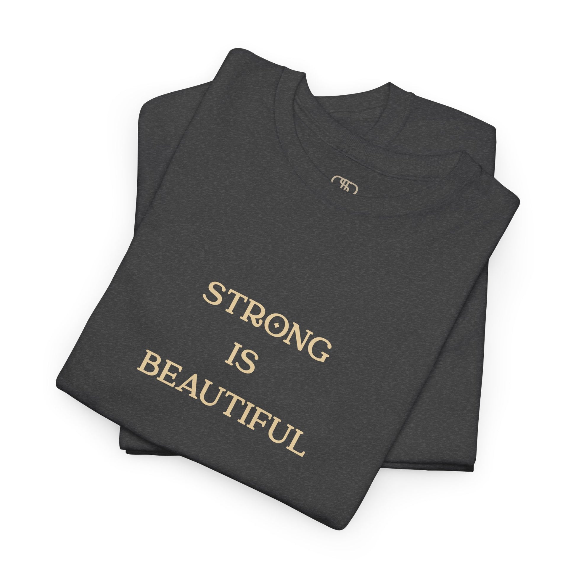 An Art Nouveau style illustration on the back of a folded heather gray t-shirt, featuring a strong woman with flowing brown hair curling a dumbbell. Below her, the words "Strong is Beautiful" are written in an elegant, stylized font, framed by intricate floral and line work.