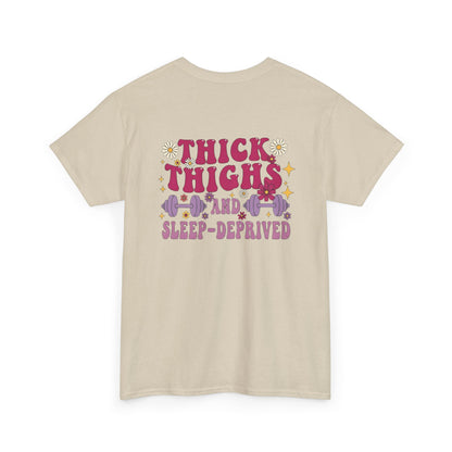 A [sand] t-shirt with the phrase "Thick Thighs and Sleep Deprived" in a retro font on the front left and enlarged on the back.