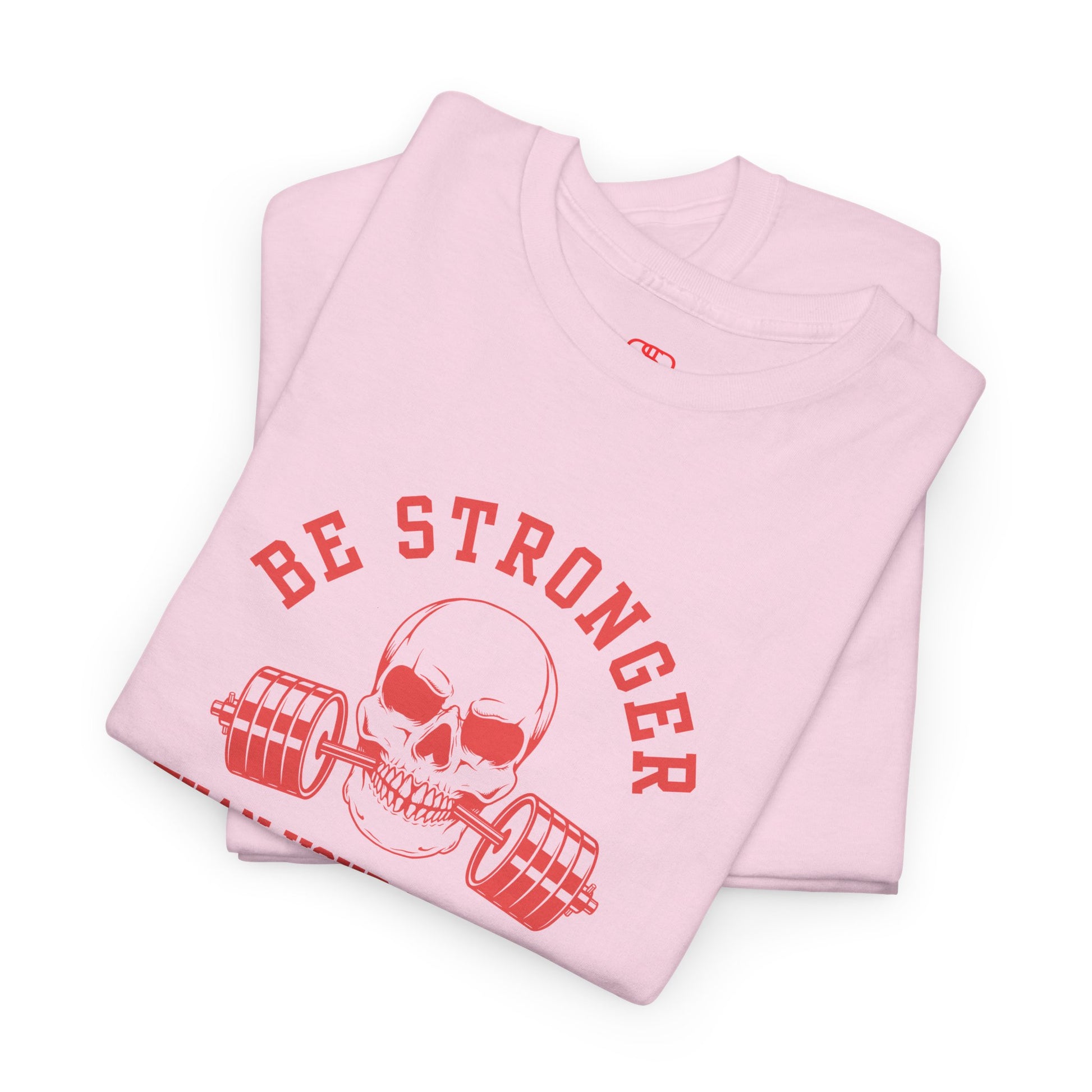 A folded t-shirt in  [light pink] with a skull biting a barbell and the words “Be Stronger Than Your Excuses.”