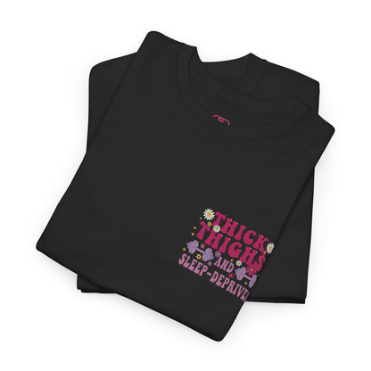 A folded [black] t-shirt with the phrase "Thick Thighs and Sleep Deprived" in a retro font on the front left and enlarged on the back.