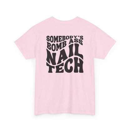 A light pink t-shirt with black text 'SOMEBODY'S BOMB ASS NAIL TECH' on a white background in a creative wavy font. 