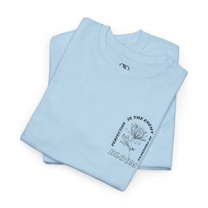 A [folded light blue] t-shirt with a central flower design and the words “Perfection is the enemy of progress” and “Bloom” underneath it the phrase "Consistent effort breeds greatness," featured on the back of the t-shirt.