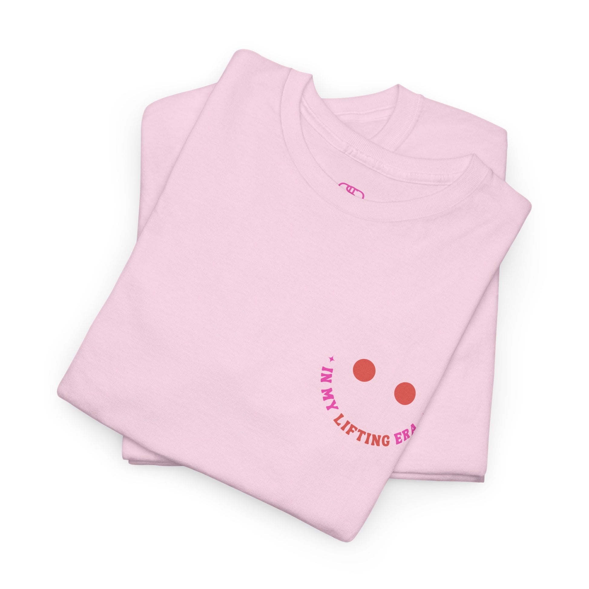 A folded pink t-shirt with a retro smiley face on the front and the phrase “In my lifting Era” in a creative retro design on the back.