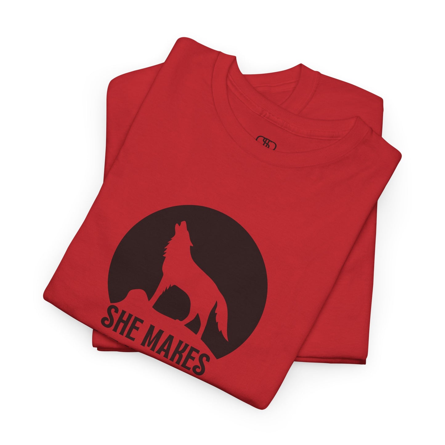 A folded red T-shirt with a wolf silhouette howling at the moon on a cliff, and "She makes me HOOWWL" text.