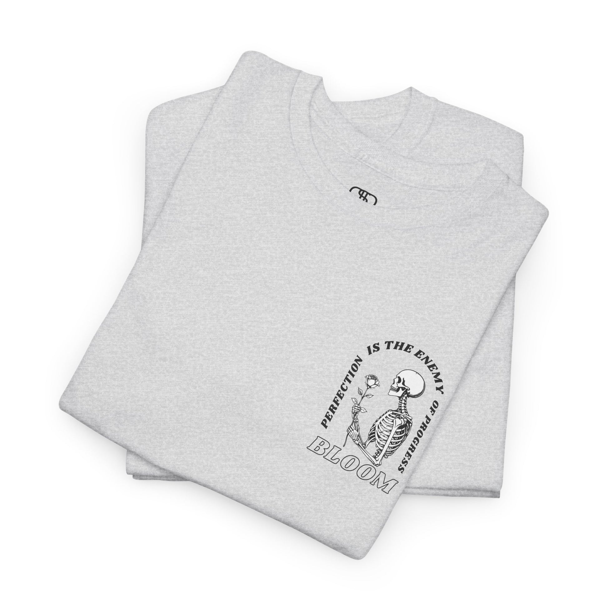 A [folded Ash Gray] t-shirt with a central skeleton and rose design and the words “Perfection is the enemy of progress” and “Bloom” on the front.