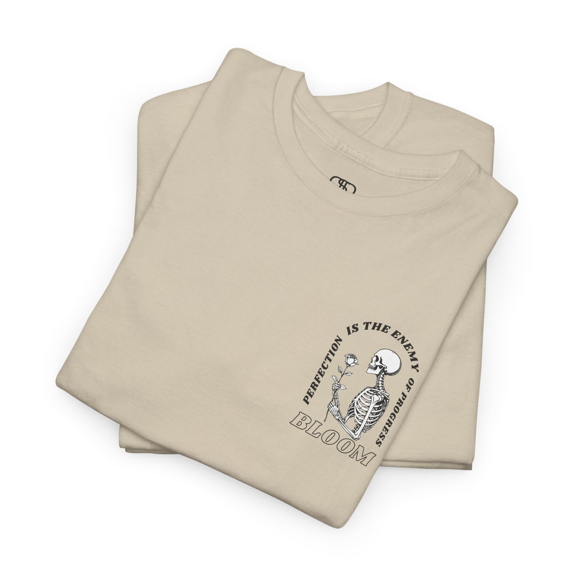 A [folded sand] t-shirt with a central skeleton and rose design and the words “Perfection is the enemy of progress” and “Bloom” on the front.