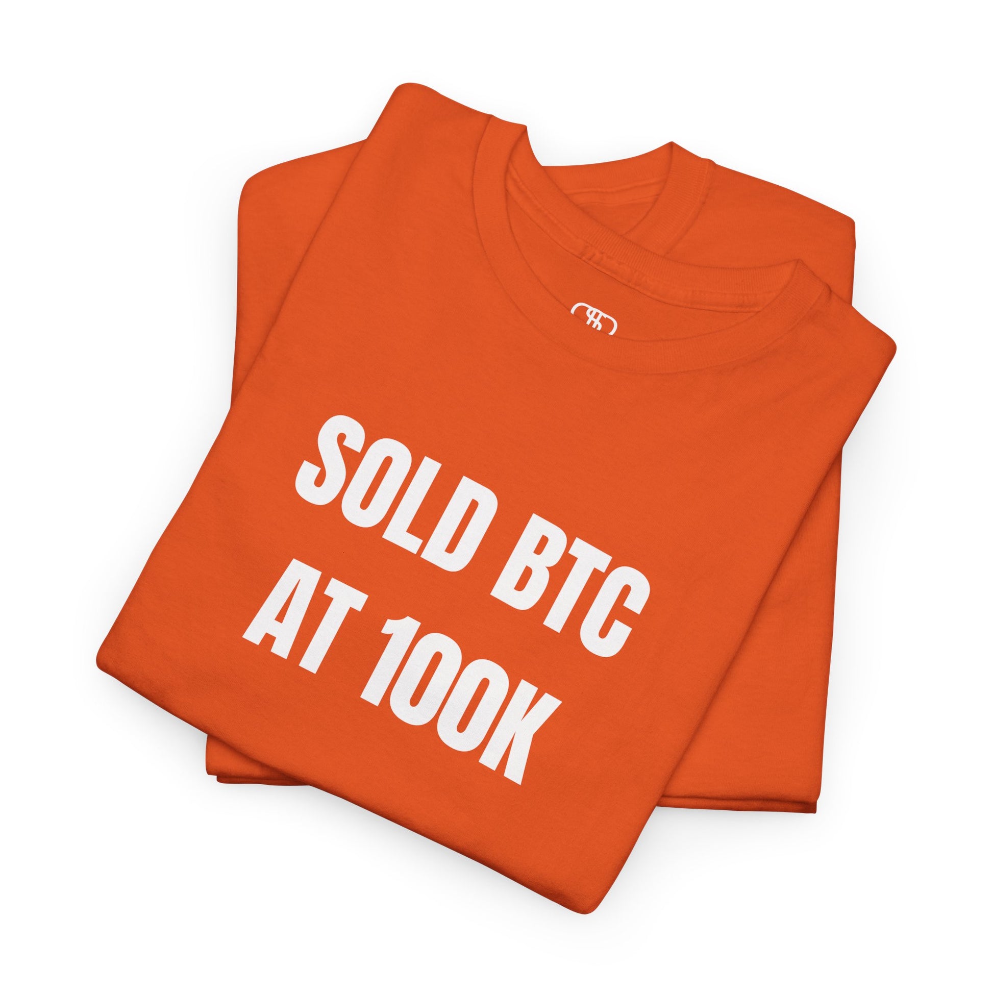 A folded orange T-shirt with bold text "SOLD BTC At 100K" on the front.