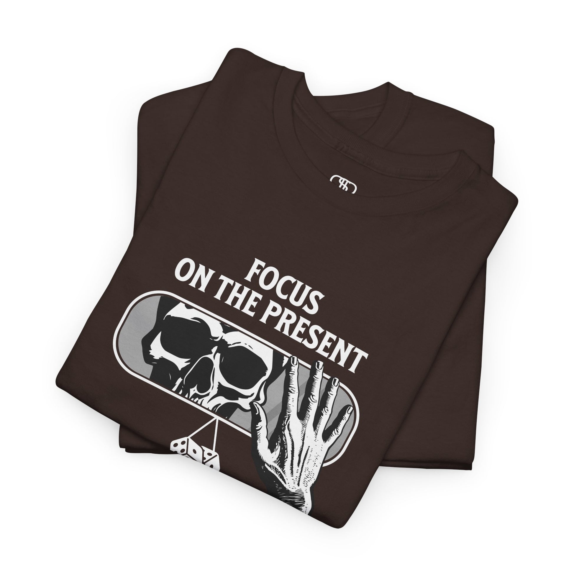 A t-shirt graphic folded of a car's rearview mirror reflecting a skeleton's face. A living hand reaches toward the mirror, which has dice dangling from it. The phrase “Focus on the present” is part of the design.
