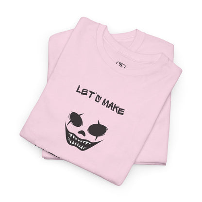 A folded light pink T-shirt with a daring clown graphic with sharp teeth and scars, and "Let’s Make Haunting Memories" text.