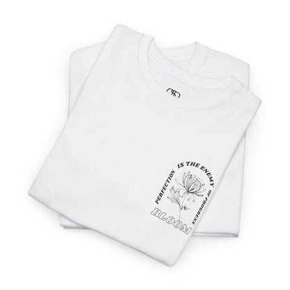 A [folded white] t-shirt with a central flower design and the words “Perfection is the enemy of progress” and “Bloom” underneath it the phrase "Consistent effort breeds greatness," featured on the back of the t-shirt.