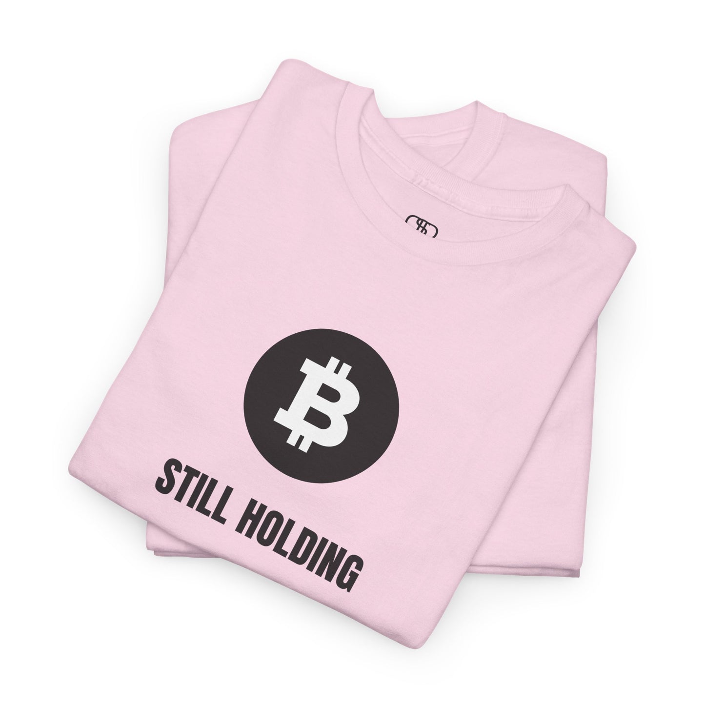 A folded light pink T-shirt with a Bitcoin emblem and "Still Holding" text in black.