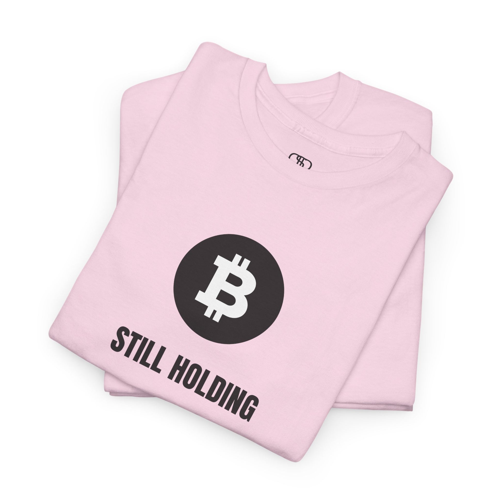 A folded light pink T-shirt with a Bitcoin emblem and "Still Holding" text in black.